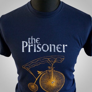 May include: A navy blue t-shirt with a white graphic of a bicycle and the text "the Prisoner".