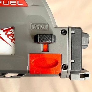 Peut inclure: Un outil électrique gris et rouge avec le texte "FUEL" et "M18" dessus. L'outil a un levier noir et un bouton rouge.
