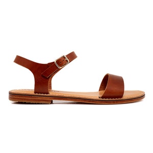 May include: Brown leather sandals with a buckle closure. The sandals have a flat sole and a simple design.