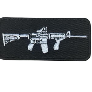Könnte beinhalten: Schwarzer rechteckiger Aufnäher mit einem weißen, gestickten Gewehrdesign. Das Gewehr ist detailliert mit Zielfernrohr, Schaft und anderen Merkmalen dargestellt. Geeignet für Jacken, Taschen oder andere Kleidungsstücke.