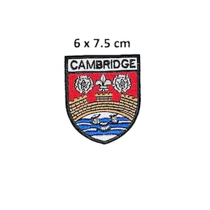 Könnte beinhalten: Gestickter Aufnäher mit dem Cambridge-Wappen. Der schildförmige Aufnäher trägt oben das Wort "CAMBRIDGE". Das Design umfasst einen roten Hintergrund, eine goldene Brücke, blaues Wasser und weiße Rosen. Der Aufnäher misst 6 x 7,5 cm.