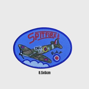 May include: Oval-shaped embroidered patch depicting a Spitfire aircraft. The patch has a blue background and a red border. The plane is olive green and brown, with the word "Spitfire" in red. The patch measures 8.5 x 6 cm.