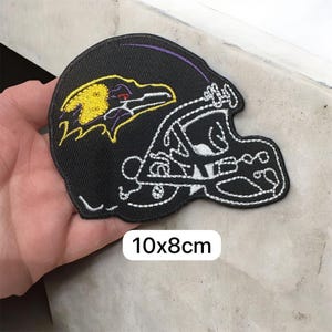 May include: Black embroidered patch with a football helmet design. The patch features a yellow and purple raven logo and white stitching. The patch measures 10x8cm, approximately 3.9x3.1 inches.