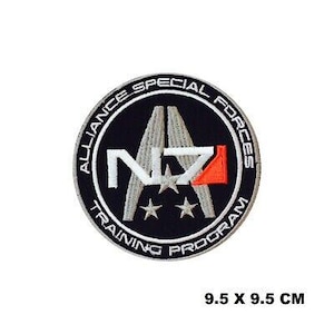 Może przedstawiać: Naszywka haftowana w kolorze czarnym i białym z tekstem "Alliance Special Forces Training Program" i literami "N7" w białym kółku. Naszywka ma 9,5 cm x 9,5 cm.