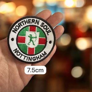 Op de afbeelding: Een ronde geborduurde patch met de tekst "NORTHERN SOUL NOTTINGHAM" in wit op een zwarte rand. Het midden toont een groene boogschutter met pijl en boog op een schild, omringd door rode en groene strepen. De patch is 7,5 cm in diameter.