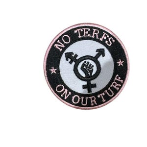May include: Circular embroidered patch with a black border and a pink edge. The patch features the text "NO TERFS ON OUR TURF". The centre has a symbol with a fist, arrows, and gender symbols.