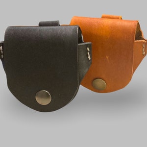 May include: Two leather coin purses, one black and one brown. Both purses have a snap closure and a small metal button on the front.