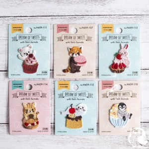 Op de afbeelding: Zes kleurrijke strijklabels met schattige dierenfiguren die van zoete lekkernijen genieten. Elk strijklabel heeft een roze achtergrond met de tekst "Dream of Sweets with Petit Animals" en een nummer. De strijklabels zijn gemaakt in Japan.