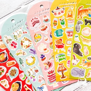 Può includere: Una collezione di fogli di adesivi colorati con varie illustrazioni. I disegni includono elementi alimentari come torte e bevande, insieme a gatti, fiori e altri elementi decorativi. Ogni foglio ha testo giapponese in alto.