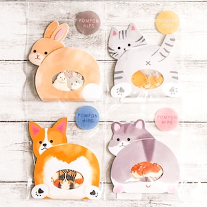 May include: Four clear plastic bags each containing a different animal shaped sticker. The stickers are of a bunny, a cat, a corgi, and a cat. Each sticker has a hole in the middle and a smaller sticker inside the hole. The smaller stickers are of different animals. The bags have a sticker on the top that says "Pompon Hips".