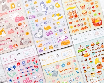 Op de afbeelding: Verschillende vellen decoratieve stickers met diverse ontwerpen. De stickers tonen honden, katten, bakkerijproducten, bloemen en briefpapier. De stickers zijn in verschillende kleuren, waaronder roze, blauw, geel en oranje.