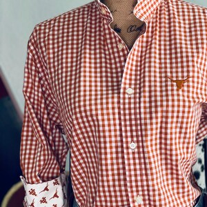 Peut inclure: Une chemise &agrave; carreaux rouge et blanc avec un col &agrave; volants et des manches longues. La chemise pr&eacute;sente un petit logo Longhorn et des poignets &agrave; motifs. La chemise est associ&eacute;e &agrave; une ceinture et un jean.