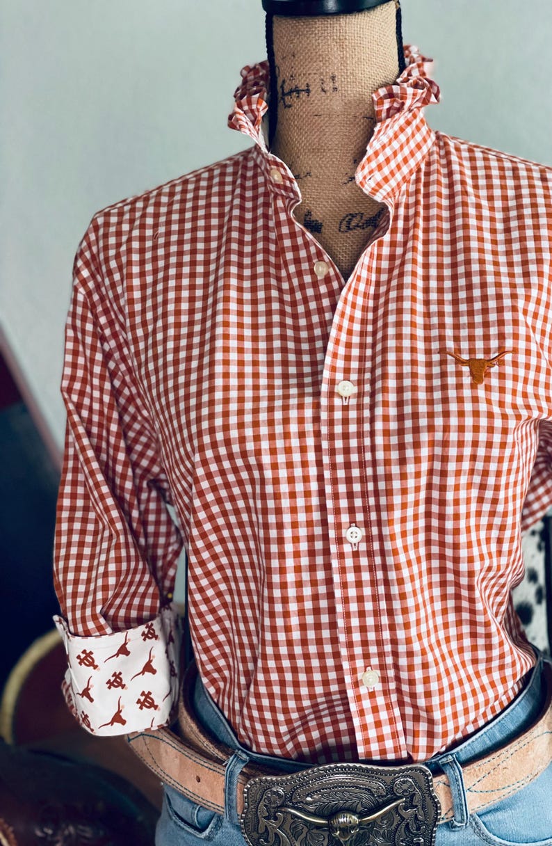 Peut inclure: Une chemise &agrave; carreaux rouge et blanc avec un col &agrave; volants et des manches longues. La chemise pr&eacute;sente un petit logo Longhorn et des poignets &agrave; motifs. La chemise est associ&eacute;e &agrave; une ceinture et un jean.