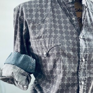 Peut inclure: Chemise grise &agrave; boutons avec un motif g&eacute;om&eacute;trique blanc. La chemise a deux poches avant, un col et les manches sont retrouss&eacute;es pour r&eacute;v&eacute;ler un poignet en jean. La chemise est pr&eacute;sent&eacute;e sur un mannequin.
