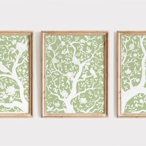 Op de afbeelding: Drie ingelijste prints met een groene achtergrond en een wit silhouet van een boom met vogels en bloemen.