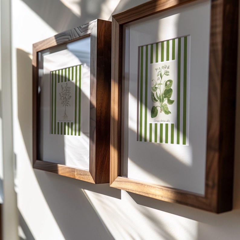 May include: Two framed botanical prints with green and white striped backgrounds. The prints feature illustrations of plants with green leaves and white flowers.