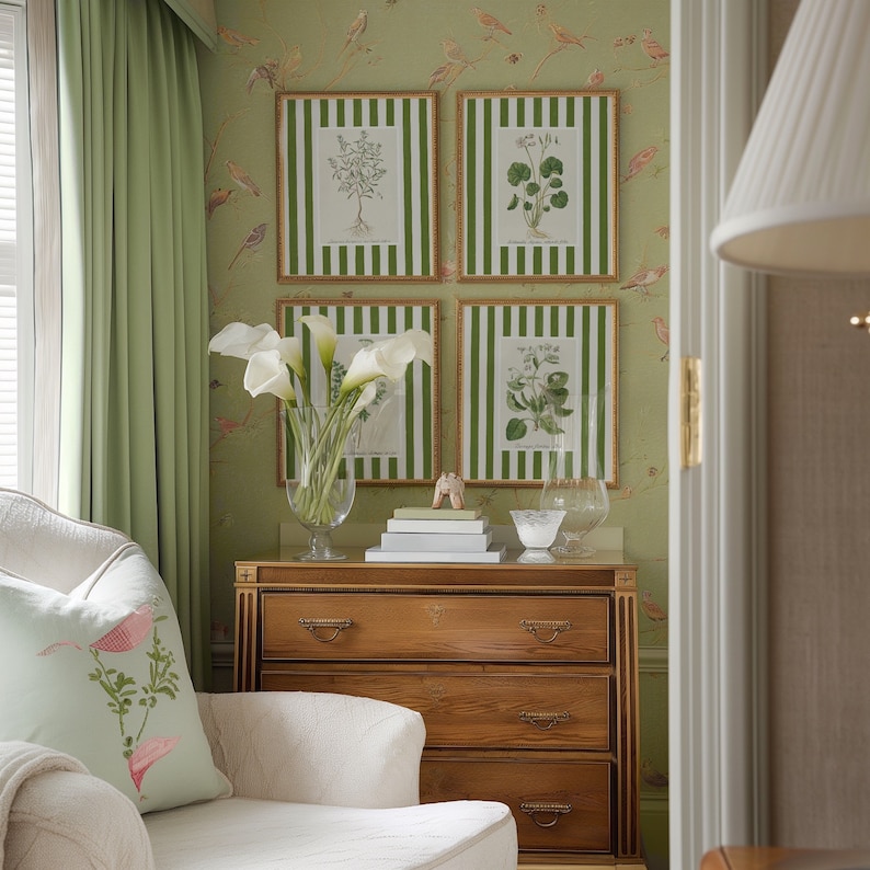 May include: A white upholstered armchair with a green floral pillow sits in front of a wooden dresser with three drawers. The dresser is against a green wall with four framed botanical prints.