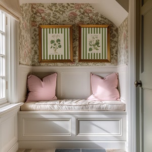 May include: A white bench with a padded seat and two pink pillows. The bench is built into a wall with white wainscoting and a floral wallpaper. Two framed botanical prints hang above the bench.