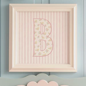 May include: A white picture frame with a pink and white striped background. The letter "B" is in the center of the frame and is covered in a floral pattern.