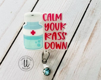 May include: A white plastic badge holder with a clear plastic vial with a red cross and blue liquid. The text "CALM YOUR KASS DOWN" is printed in red on the badge holder.