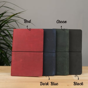Peut inclure: Quatre journaux reli&eacute;s en cuir de couleur rouge, bleu fonc&eacute;, vert et noir. Les journaux sont munis de fermetures &eacute;lastiques et sont dispos&eacute;s en rang&eacute;e sur une surface en bois.