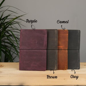 Peut inclure: Quatre journaux reli&eacute;s en cuir de couleur pourpre, marron, camel et gris. Les journaux sont ferm&eacute;s et ont un design simple.