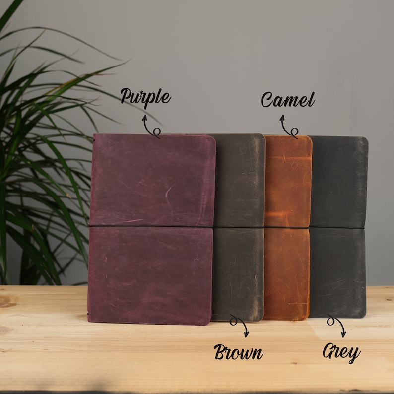 Peut inclure: Quatre journaux reli&eacute;s en cuir de couleur pourpre, marron, camel et gris. Les journaux sont ferm&eacute;s et ont un design simple.