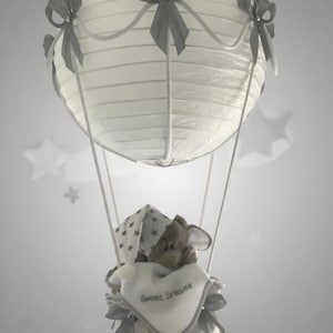 May include: A white paper lantern hot air balloon with grey bows and ribbons. A teddy bear wearing a star-patterned hat and a bib that says "Sweet Dreams" is in the basket. Nursery decoration.
