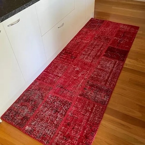 May include: A red and white patchwork runner rug with a distressed look. The rug is made of different pieces of fabric sewn together.