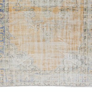 May include: A vintage rug with a faded, light brown background and a blue and green border. The rug has a distressed look and features a floral pattern.
