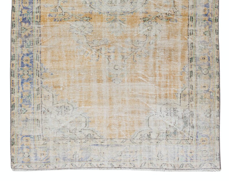 May include: A vintage rug with a faded, light brown background and a blue and green border. The rug has a distressed look and features a floral pattern.
