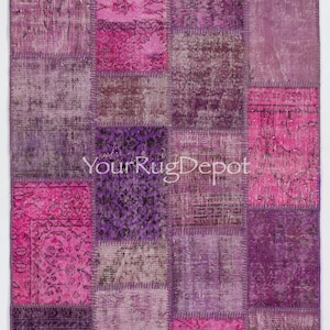 May include: A patchwork rug with a variety of purple and pink hues. The rug is made up of different squares of fabric, each with a unique pattern. The rug has a vintage look and feel.