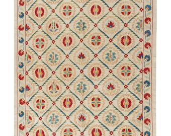 May include: A white cotton rug with a repeating pattern of red, blue, and yellow floral motifs. The rug has a diamond-shaped grid pattern with a floral design in each square.