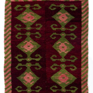 May include: A red, green, and pink patterned rug with a white fringe. The rug has a geometric design with repeating diamond shapes.
