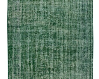 Op de afbeelding: Een rechthoekig, verweerd groen tapijt met een vervaagde, getextureerde uitstraling. Het tapijt heeft een dicht, geweven patroon met variaties in de groene kleur, wat een vintage look creëert. De randen zijn afgewerkt met een lichtgekleurde franje.