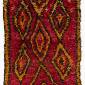 Könnte beinhalten: Ein roter, orangefarbener und schwarzer Teppich mit Fransen. Der Teppich hat ein geometrisches Muster mit einer Diamantform in der Mitte.