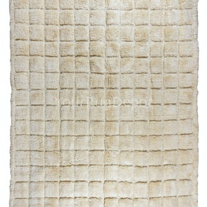 Peut inclure: Un tapis moelleux de couleur crème avec un motif carré. Le tapis a une texture douce et moelleuse et est fait d'un matériau de haute qualité.