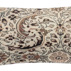 Puede incluir: Cojín rectangular decorativo con un intrincado estampado floral en crema, marrón y negro. El cojín presenta un diseño detallado de estilo vintage con un borde a lo largo de los bordes. La estética general recuerda a una alfombra tradicional.