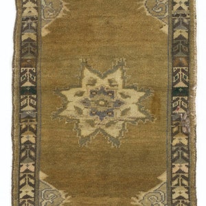 May include: A small, rectangular rug with a brown background and a central starburst design in shades of blue, green, and white. The rug has a border with geometric patterns in brown, blue, and white.
