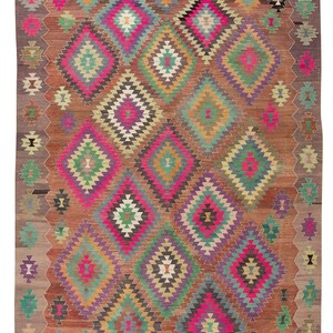 May include: A colourful rug with a geometric pattern of diamonds and squares in shades of pink, green, purple, brown, and beige. The rug has a fringed border.