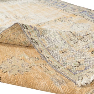 May include: A vintage rug with a faded, light brown background and a blue and green floral pattern. The rug has a frayed edge and is folded in half.