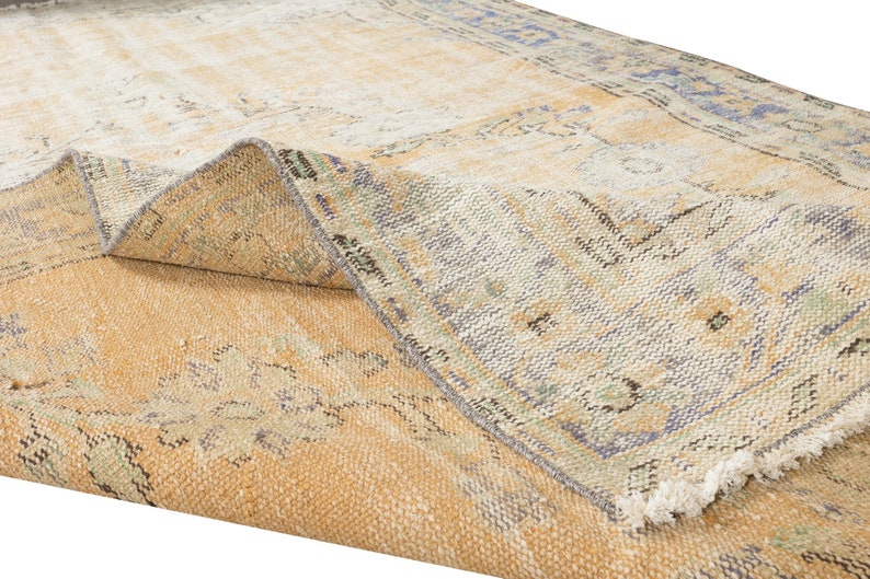 May include: A vintage rug with a faded, light brown background and a blue and green floral pattern. The rug has a frayed edge and is folded in half.
