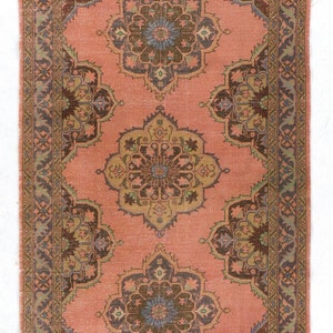 Puede incluir: Una alfombra rosa vintage con un patrón repetido de intrincados diseños florales en tonos marrones, verdes y azules. La alfombra tiene un borde con un patrón floral similar.