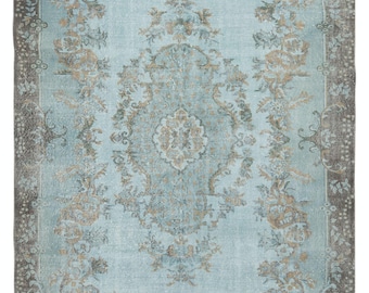 Puede incluir: Una alfombra vintage con fondo azul claro y un patrón floral en tonos marrones y grises. La alfombra tiene un aspecto desgastado y una apariencia descolorida.