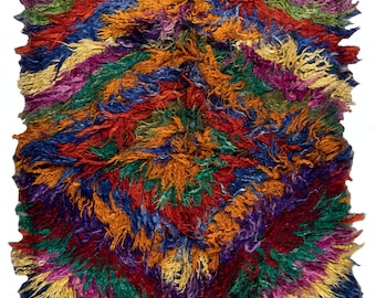 Peut inclure: Un tapis coloré tissé à la main avec un design abstrait unique. Le tapis présente une variété de couleurs, notamment le rouge, l'orange, le jaune, le vert, le bleu et le violet. Le tapis a une texture hirsute et est fait de laine.