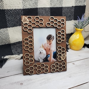 May include: A wooden picture frame with a honeycomb design and bee accents. The frame is brown and has a photo of a child and a dog inside.