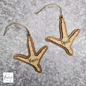 May include: Two wooden ornaments shaped like a chicken foot. The ornaments are personalized with the names "Karen" and "Squirt".