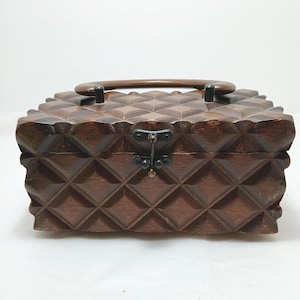 May include: A vintage wooden box with a geometric diamond pattern carved into its surface. The box has a dark brown finish, a curved wooden handle, and a metal clasp. The box is likely used for storage or as a decorative item.