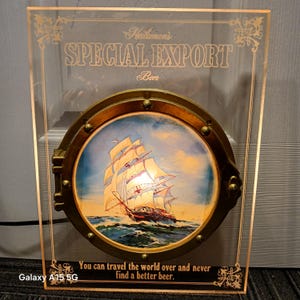 May include: A clear acrylic sign with gold lettering that reads "Heileman's SPECIAL EXPORT Beer." A round, brass-colored porthole features a painting of a sailing ship on the ocean. The text "You can travel the world over and never find a better beer" is at the bottom.