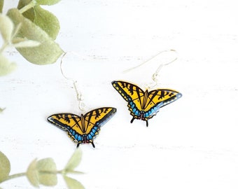 May include: A pair of silver dangle earrings featuring a yellow and black butterfly design with blue accents. The butterflies are made of resin and have a realistic appearance.